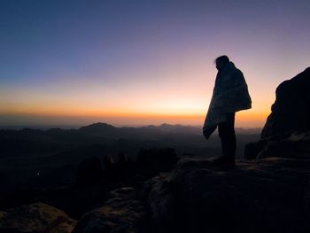 Rear view of man standing on rock against sky during sunset