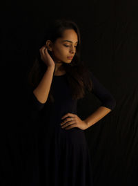 Young woman looking down while standing against black background