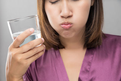 Close-up of woman drinking water while standing against wall