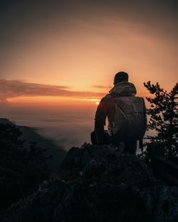 Rear view of man standing on rock against sky during sunset