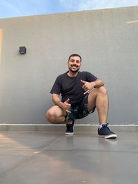 Portrait of young man sitting against wall