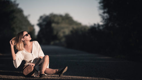 Young woman sitting on road against trees