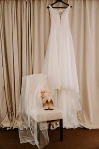 Wedding dress hanging on coat hanger against brown curtain