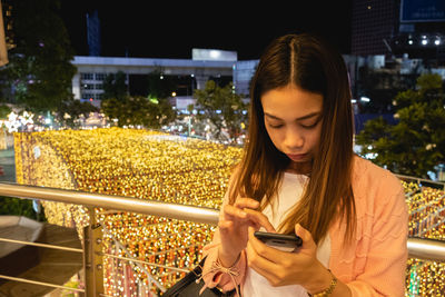 Young woman using mobile phone while standing at camera