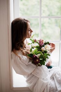 Young woman sitting with flowers on window at home