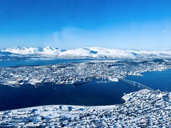 Scenic view of city island below snowcapped mountains against blue sky