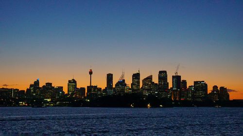 Illuminated buildings in city against clear sky during sunset