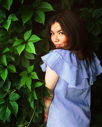 Portrait of young woman standing by plants