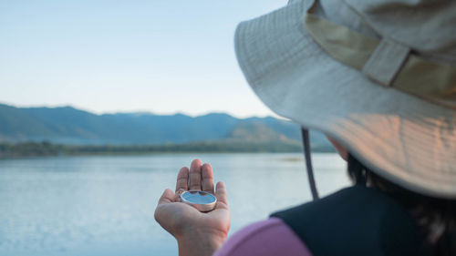 Rear view of woman holding compass looking at lake