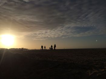 Silhouette men on landscape against sky during sunset