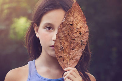 Close-up portrait of cute beautiful girl holding dry leaf in park