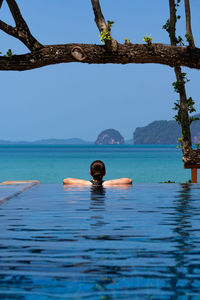 Young woman wearing bikini standing in the blue infinity swimming pool looking at the view of ocean