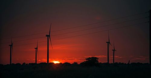 Silhouette electricity pylons on field against orange sky