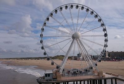 Ferris wheel at beach against cloudy sky