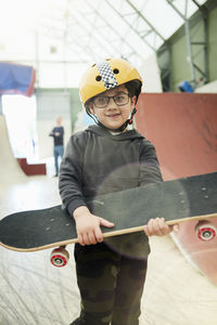 Portrait of boy holding skateboard in indoor skatepark