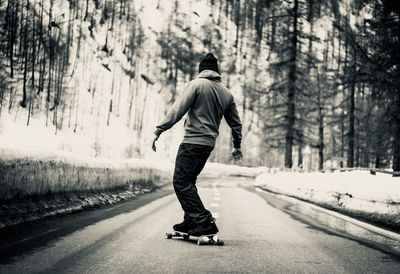 Rear view of man skateboarding on road during winter