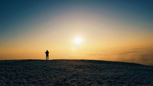 Silhouette of man standing on field against sky during sunset