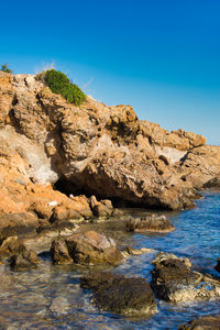 Rock formations by sea against clear blue sky