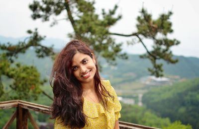 Portrait of smiling young woman against trees