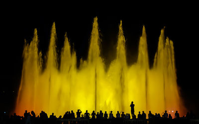 Silhouette of people at night in front of a fountain