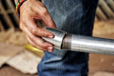 Close-up of manual worker holding metallic pipe outdoors