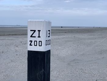 Text on wooden post at beach against sky