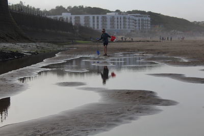 Boy standing on shore against sky