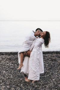 Rear view of couple kissing on sea shore against sky