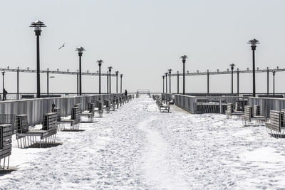 Empty snow covered walkway by benches against clear sky