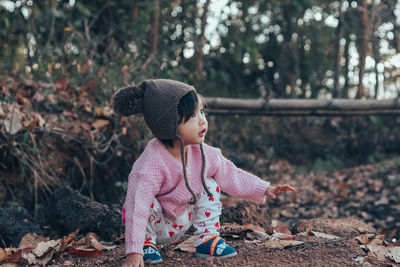 Cute baby girl looking away while crouching on land during winter