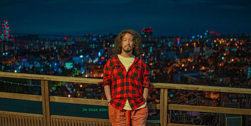 Portrait of young man standing against railing in city at night