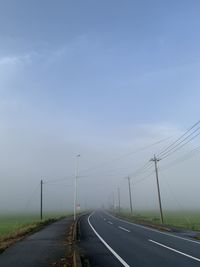 Road by electricity pylon against sky