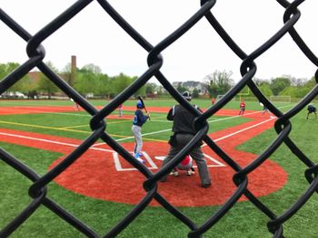 People standing on field seen through chainlink fence