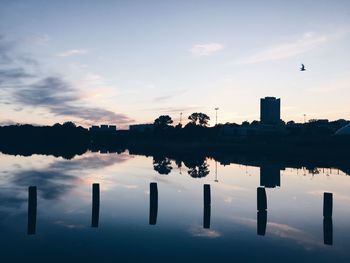 Silhouette wooden posts in lake against sky during sunset