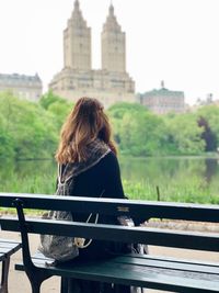 Rear view of woman sitting on railing against sky