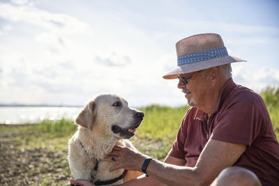 Senior man wearing hat stroking golden retriever on sunny day