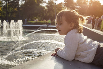 Adorable toddler girl looks at the fountains in the park in the park on a sunny day