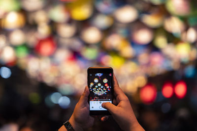 Cropped hands of woman photographing illuminated lanterns at night