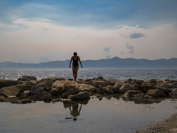 Woman standing on rock at beach against sky