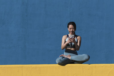 Portrait of smiling young woman sitting against wall