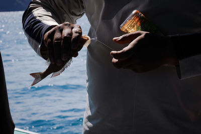 Midsection of fisherman holding fish against sea