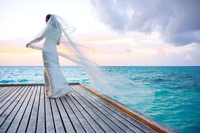 Rear view of bride standing on floorboard over sea against sky