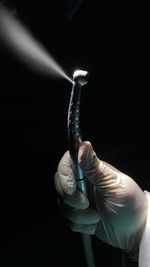 Close-up of hand holding light bulb against black background