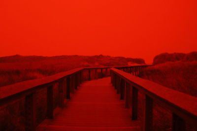 Empty footpath leading to red against clear sky