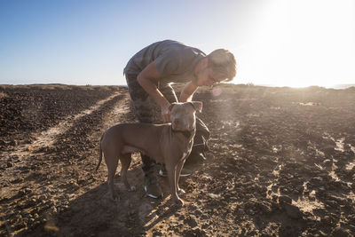 Side view of young man with dog standing at beach during sunny day