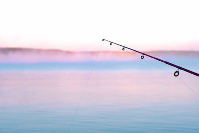 Fishing rod over sea against sky during sunset