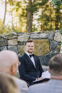 Minister holding book against wall looking at guests in wedding