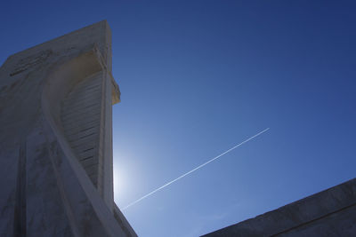 Low angle view of vapor trail against clear blue sky with statue