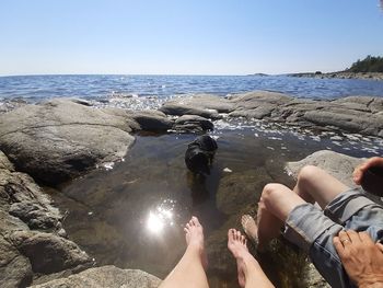 Low section of people on rocks by sea against sky