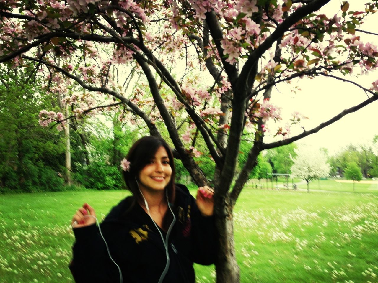 tree, lifestyles, leisure activity, young adult, young women, person, park - man made space, smiling, flower, growth, grass, casual clothing, looking at camera, green color, branch, nature, portrait, front view